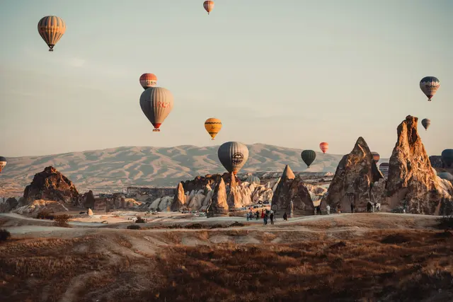 Kapadokya'da (Nevşehir) gün doğumunda peri bacaları vadisinin üzerinde süzülen onlarca rengarenk sıcak hava balonu; altın rengi ışıkta uzanan tüf kayalar ve arkadaki dağlar.