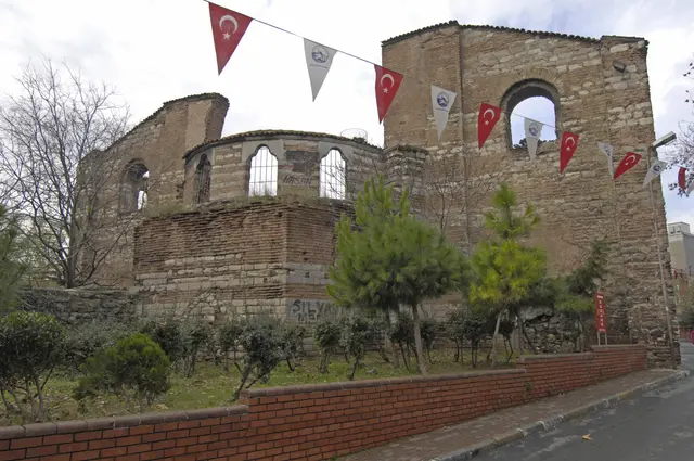 Fatih'te İmrahor İlyas Bey Camii'nin doğu ucu; taş ve tuğla bantlı çokgen apsis, üstünde kemerli pencereli yuvarlak kasnak, sağda yüksek duvar ve önde bayraklar.