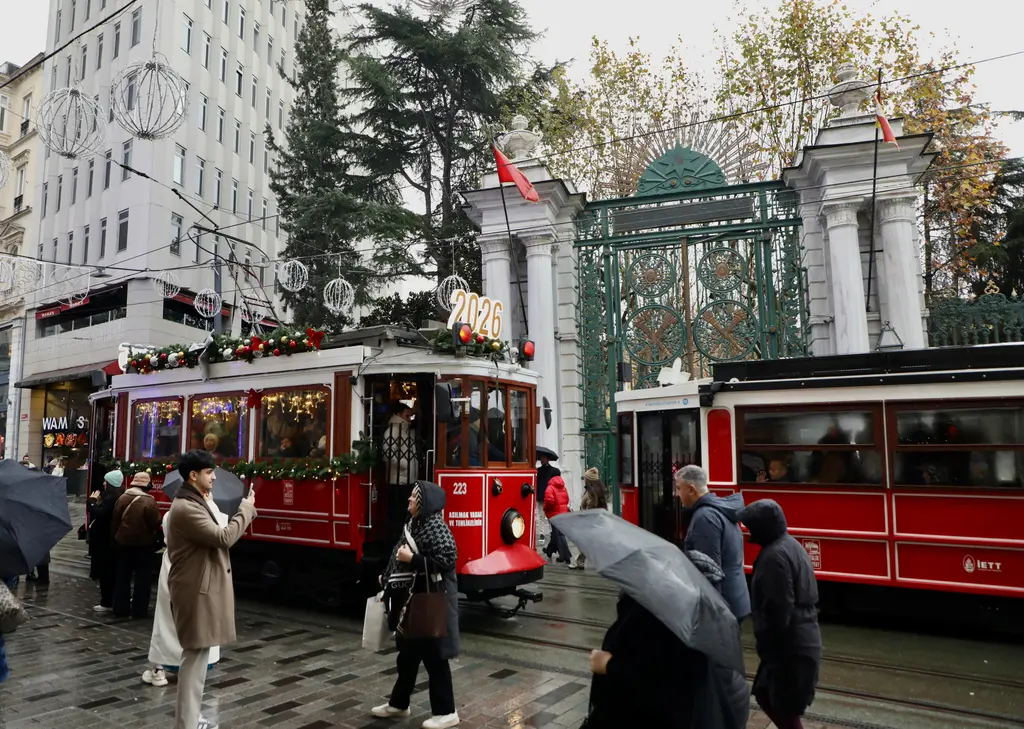 Galatasaray Lisesi'nin demir kapısı önünde süslenmiş iki kırmızı tramvay; şemsiyeli yayalar ve kapının arkasında ağaçlar.