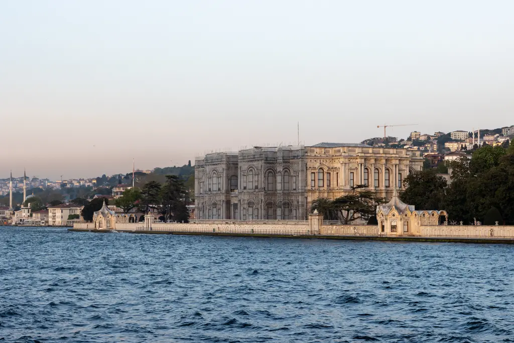 Boğaz kıyısında Beylerbeyi Sarayı; akşamüstü ışığında uzun deniz cephesi, sağda deniz köşkü ve arkada yamaçtaki evler.
