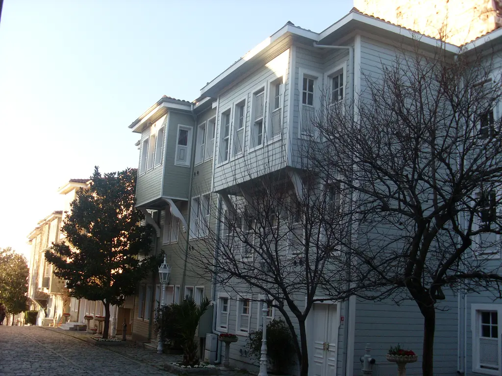 Soğukçeşme Sokağı'nda beyaz ve açık gri ahşap evler; çıkma katlar, sıra sıra pencereler, yapraksız ağaçlar ve açık gök.