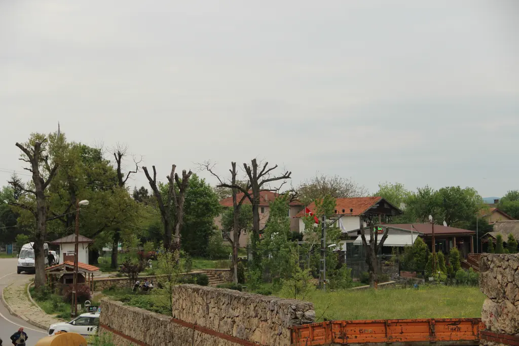 Polonezköy'de kiremit çatılı alçak evler, budanmış ağaçlar, taş duvarlı bahçe ve yol kenarında park etmiş araçlar.