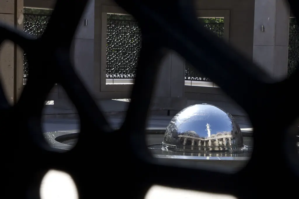 Şakirin Camii'nde kafes ardından şadırvan; ön planda koyu renkli geometrik kafes, ortasında parlayan çelik küre.