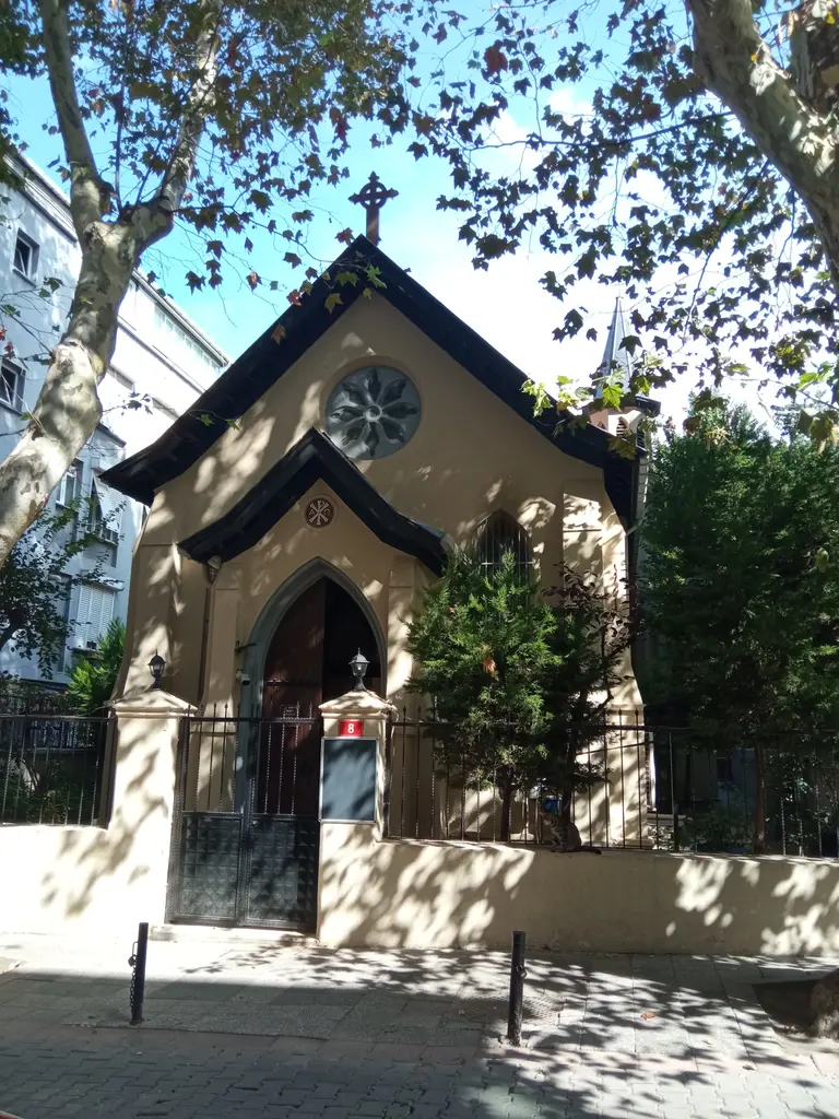 All Saints Moda Kilisesi; sivri çatılı taş yapı, kemerli giriş, saat ve çevresinde ağaçlar ile çit.