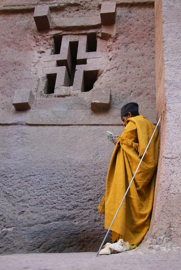Etiyopya'da Lalibela'nın kayaya oyulmuş kilisesi; haç biçimli pencere ve duvara yaslanmış, sarı pelerinli, değneği ve dua kitabıyla bir Ortodoks rahip.