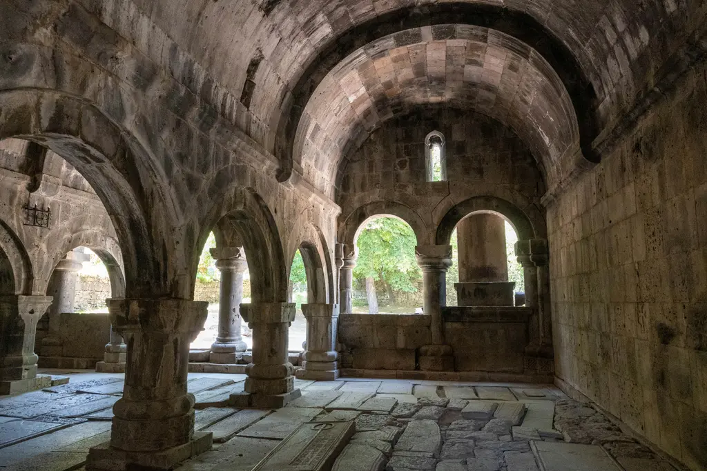 Sanahin Manastırı'nın iç mekânı; kalın taş sütunlara oturan sivri kemerler, tonozlu tavan, dışarıya açılan kemerli boşluklardan giren yeşil ışık ve zemini kaplayan oymalı mezar taşları.