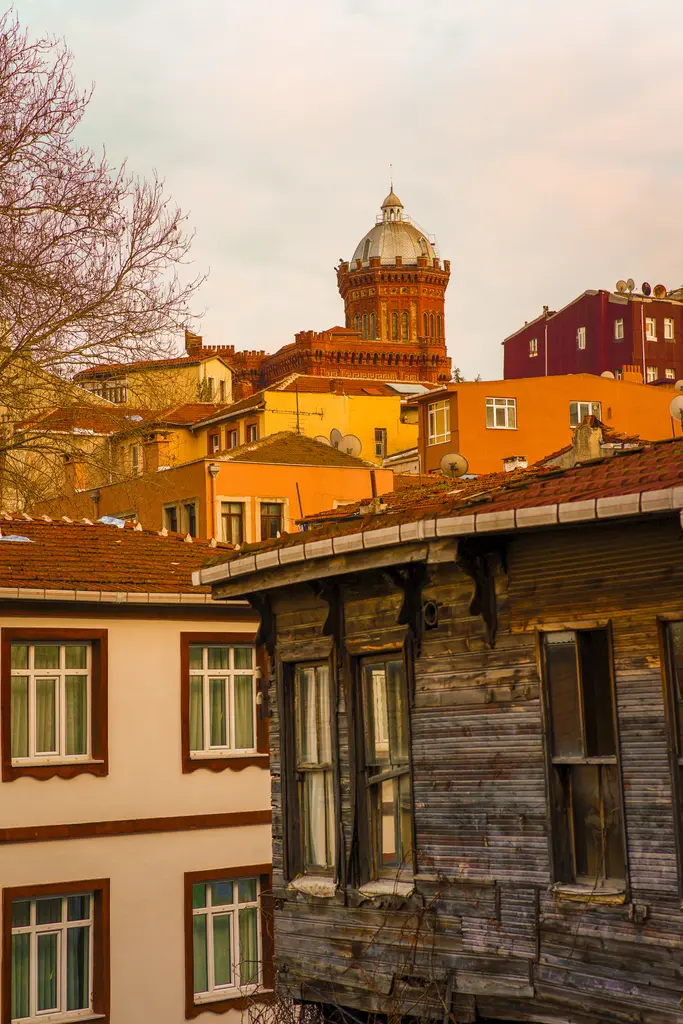 Akşam ışığında okul; turuncuya dönen tuğla cephe, önde mahallenin evleri ve karanlıklaşan gökyüzü.