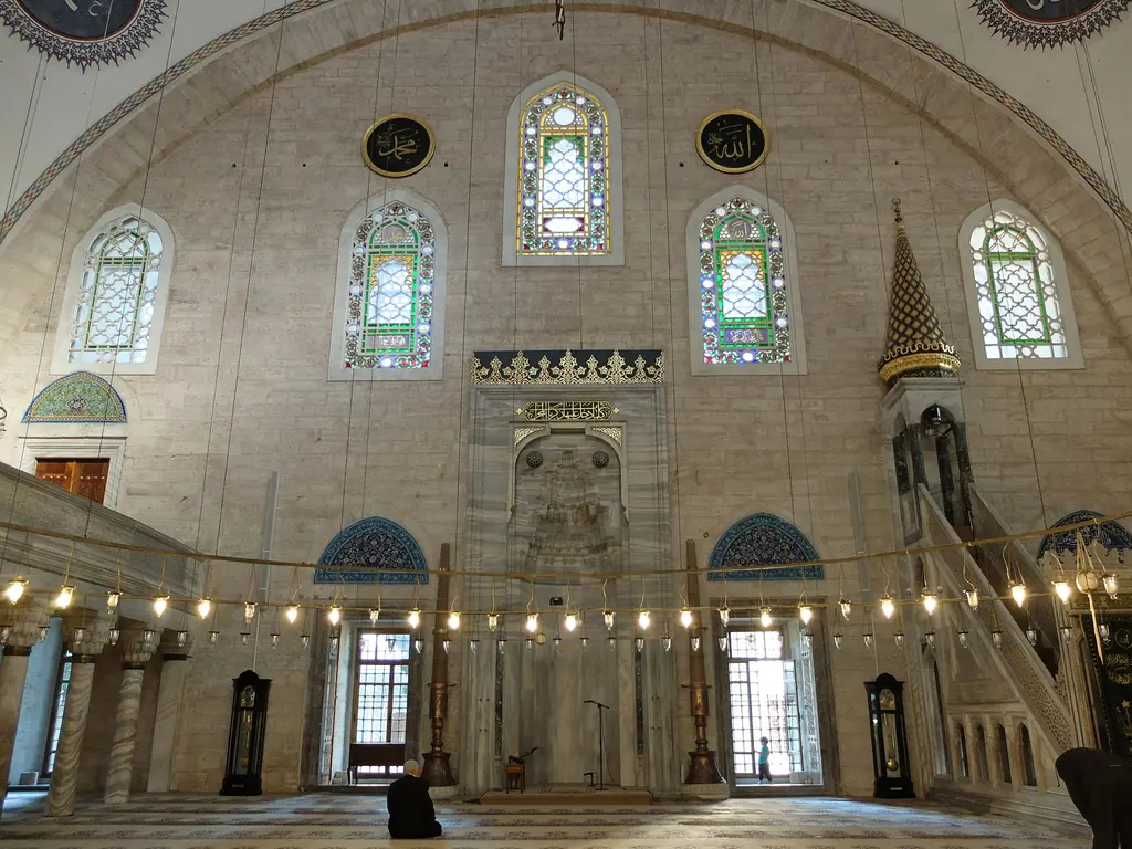 Yavuz Sultan Selim Camii'nin harimi; mihrap duvarı, sağda mermer minber, renkli camlı alçı pencereler, alınlıklarda çini panolar ve alçak avize halkası.