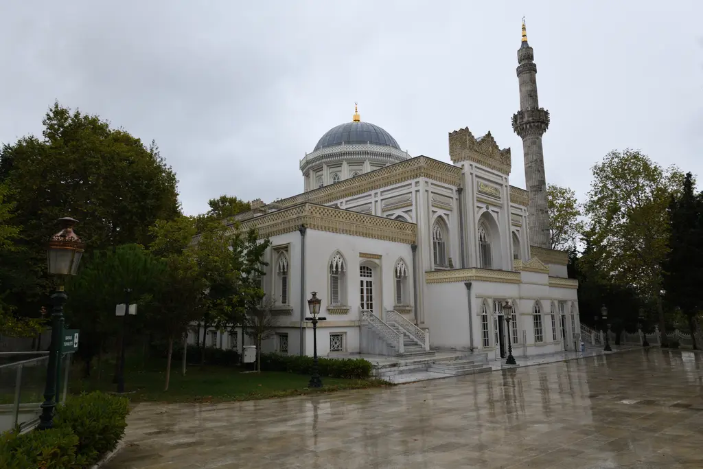 Yıldız Hamidiye Camii'ne çapraz bakış; yüksek kasnaklı kubbe, yivli ince minare, yan kanat ve önde fener direkleri.
