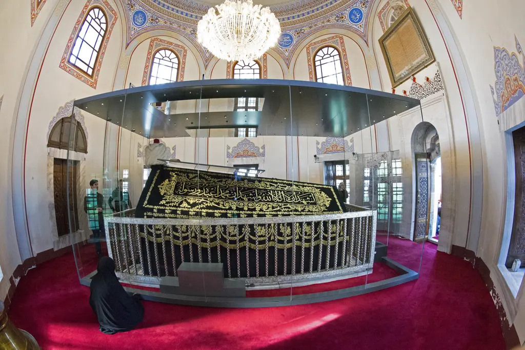 Yavuz Sultan Selim Türbesi'nin içi; kırmızı halı üstünde pirinç şebekeyle çevrili büyük sanduka, kubbede kalem işi, kristal avize ve renkli camlı pencereler.