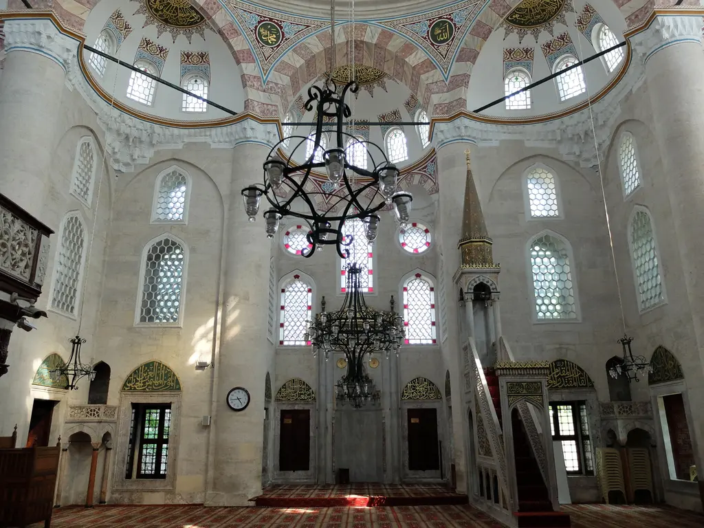 Nişancı Mehmed Paşa Camii'nde kıble duvarı; mermer mihrap, sağda minber, renkli camlı üst pencereler ve ortada asılı büyük demir avize.