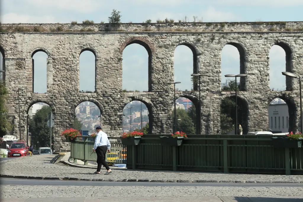 Bozdoğan Kemeri cepheden orta mesafede; dört büyük alt kemer ve üstlerinde dar gözler, ortadaki boşluktan uzakta bir cami kubbesi, önde yeşil korkuluk ve kırmızı çiçek saksıları.