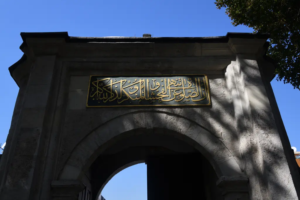 Selimiye Camii'nin avlu kapısı; kemerli taş kapı, üstünde altın harfli yazı kuşağı ve arkada ağaçlar.