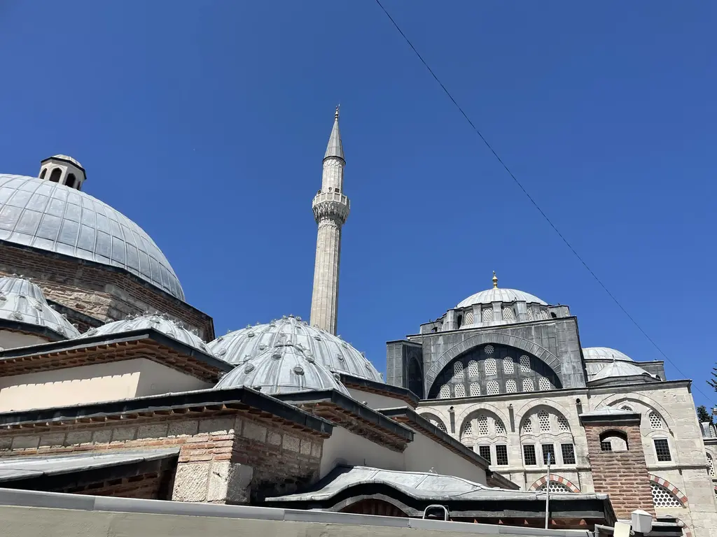 Kılıç Ali Paşa Hamamı'nın kubbeleri; tepe pencereli büyük kurşun kubbe, yanında daha küçük kubbeler, arkada caminin minaresi ve kubbe silueti.