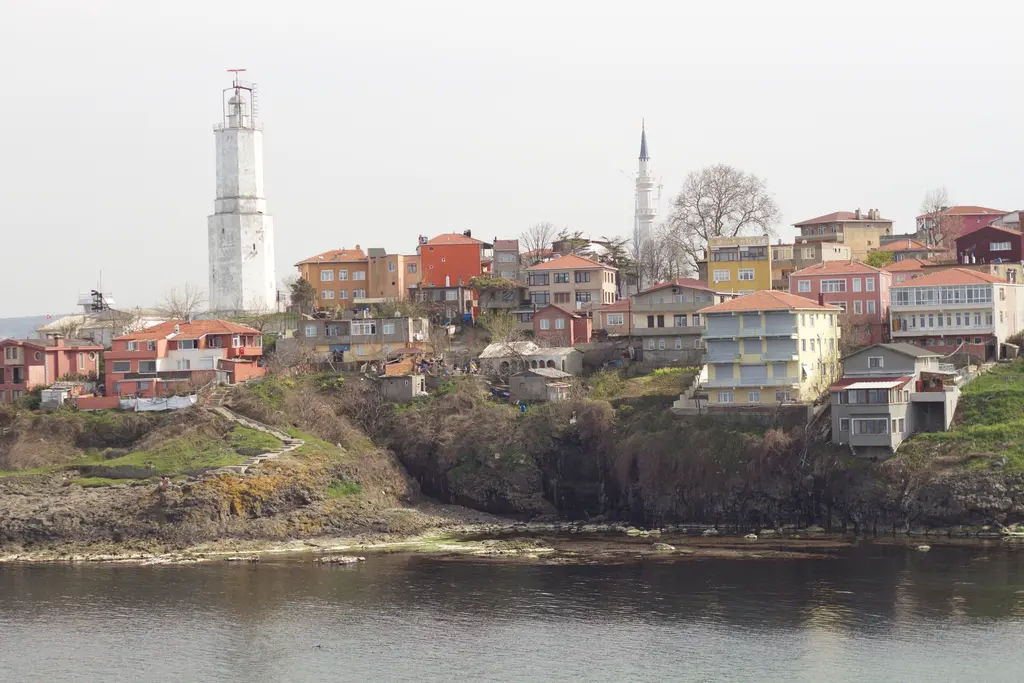 Rumelifeneri köyü; kayalık kıyıda kırmızı, sarı ve turuncu evler, yükselen beyaz fener kulesi ve minare.