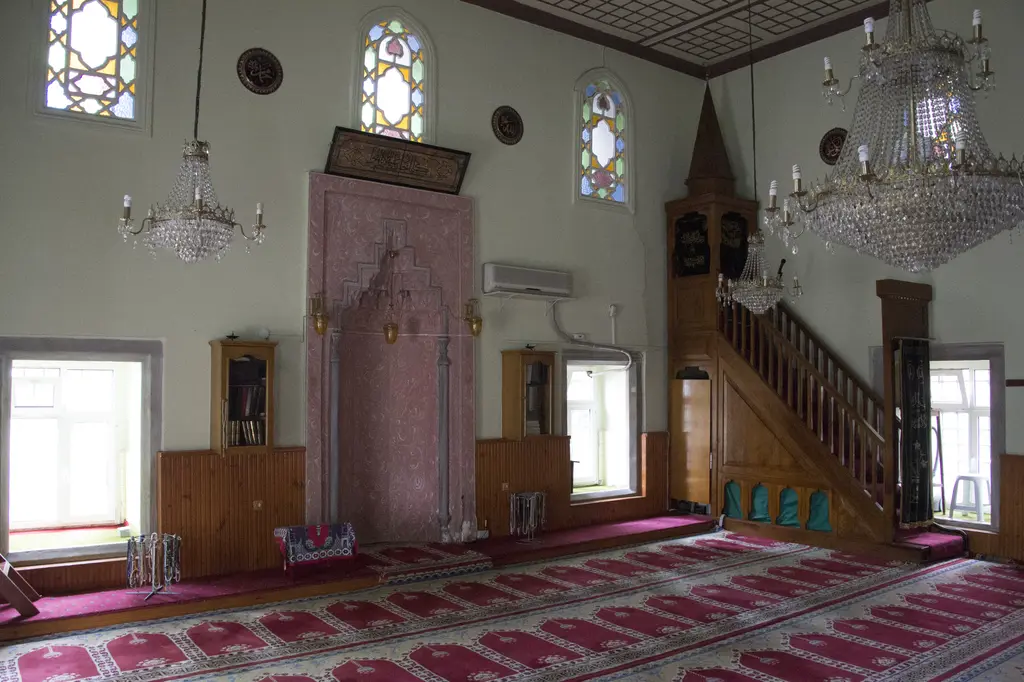 Defterdar Camii'nin harimi; pembe mermer mihrap, ahşap minber, avize, renkli camlı pencereler ve kırmızı halı.