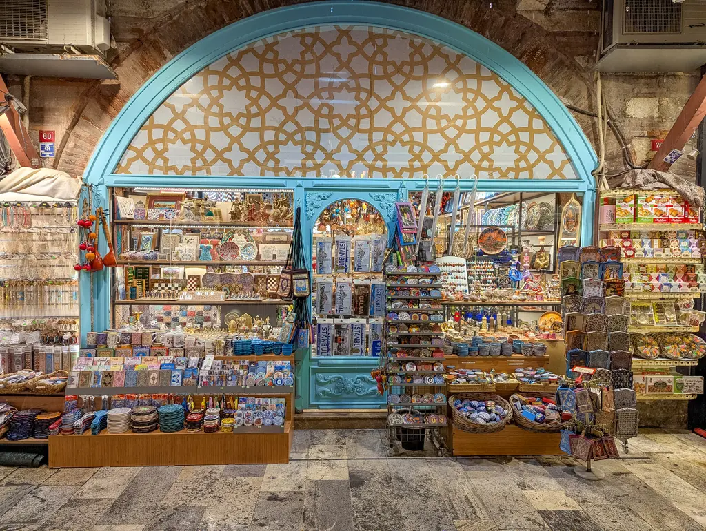 Arasta Çarşısı'nda turkuaz çerçeveli kemerli dükkân; kemerin içinde geometrik desenler, rafta seramik kâseler, lambalar ve hediyelik eşyalar.