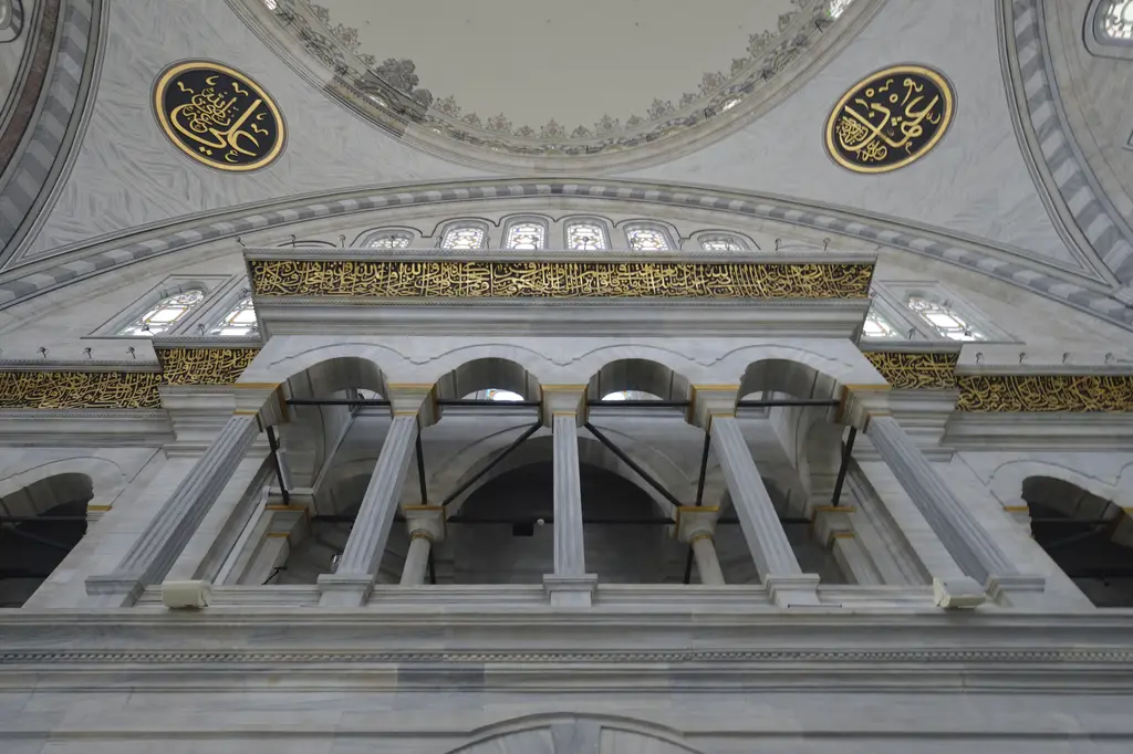 Nuruosmaniye Camii'nde mermer sütunlara oturan üst mahfil kemerleri alttan; üstte yaldızlı kuşak yazısı ve iki büyük hat madalyonu, beyaz gri mermer yüzeyler.