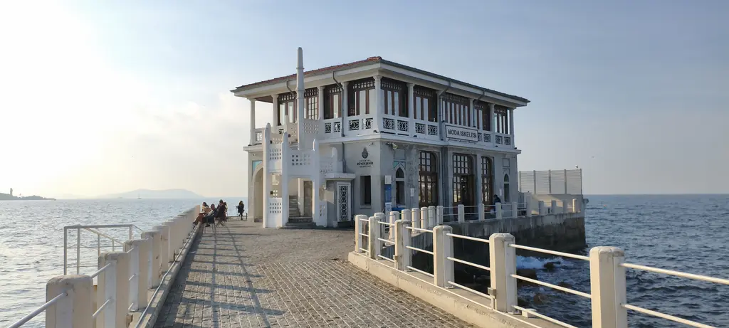 Moda İskelesi'ne giden taş yol; beyaz korkuluklar, uçta beyaz merdivenli bina ve iki yanda deniz.