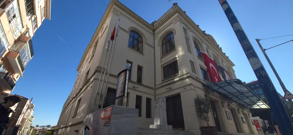 Süreyya Operası aşağıdan; mavi gökyüzüne yükselen köşe cephesi, kemerli pencereler, bayrak ve giriş saçağı.