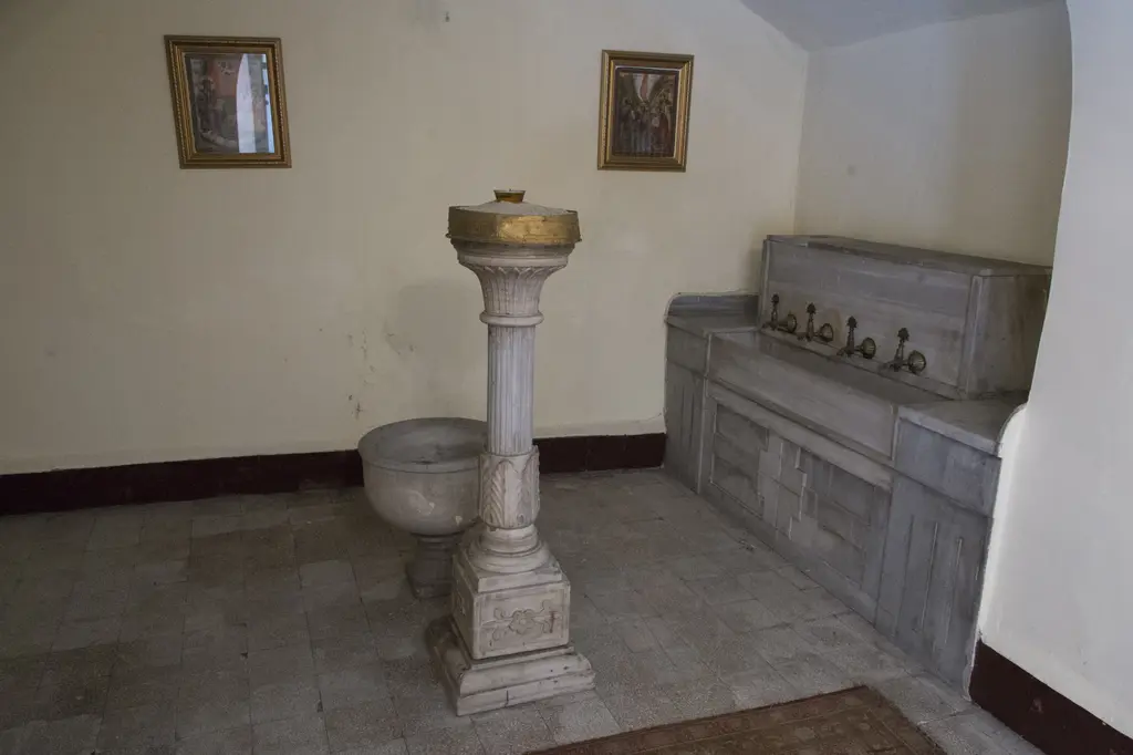 Panayia Balino Kilisesi'nde mermer vaftiz kurnası; sütun ayaklı yuvarlak kurna, yanında musluklu mermer tekne ve duvarda iki küçük ikona.