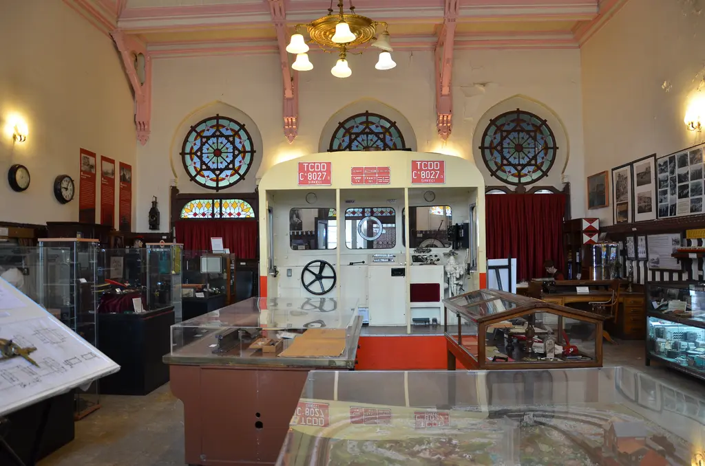 Sirkeci Garı'nda İstanbul Demiryolu Müzesi'nin salonu; ortada krem kırmızı tren sürücü kabini maketi, arkasında üç vitraylı gül pencere, iki yanda cam vitrinler ve tavanda pirinç avize.