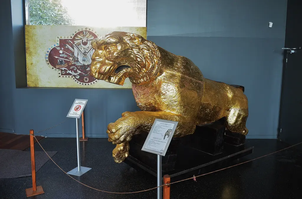 İstanbul Deniz Müzesi'nde yaldızlı aslan figürü; atılmaya hazır duruşta altın renkli aslan, kaide ve arkada bilgi panosu.