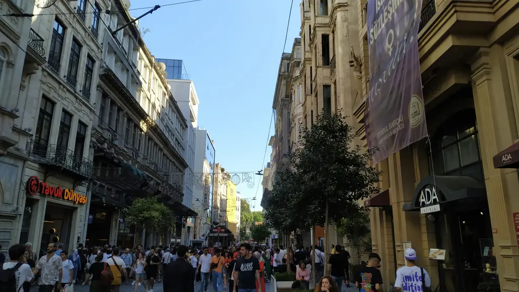 İstiklal Caddesi'nde yürüyen kalabalık; iki yanda sıralanan eski apartmanlar, mağaza vitrinleri ve caddenin üstünde asılı ışıklı süsler.