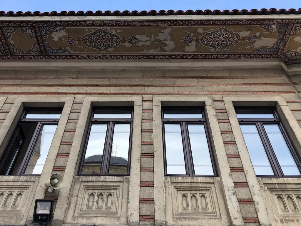 Şişli Camii'nin kütüphane binası; kırmızı çizgili taş cephe, sıralı pencereler, alt kısımda kabartma panolar ve boyalı saçak.