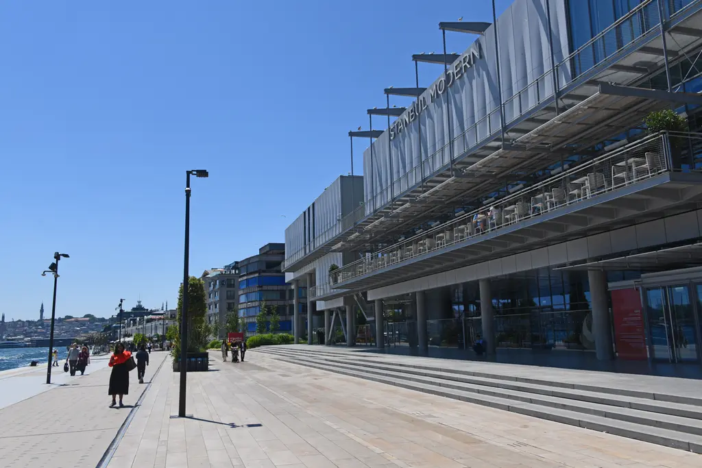 İstanbul Modern'in Boğaz'a bakan cephesi; üst katlarda terasa çıkan çelik merdivenler, önde geniş taş rıhtım ve deniz.