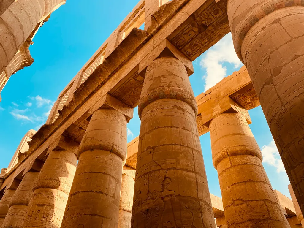 Mısır'da Luksor'daki Karnak Tapınağı'nın büyük sütunlu salonu; hiyeroglif kabartmalarla bezeli devasa sütunlar, mavi gökyüzüne doğru alttan bakış.