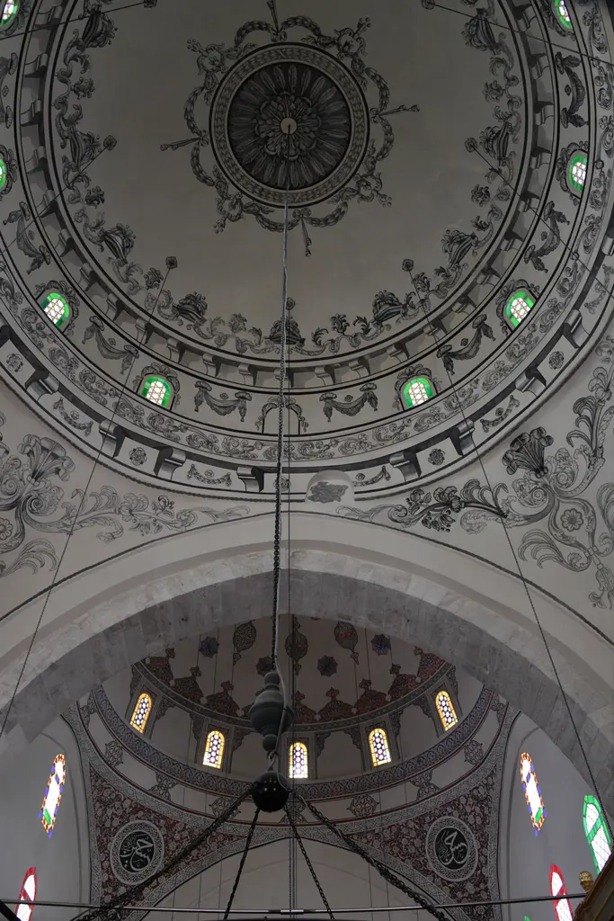 Mahmut Paşa Camii'nin iki büyük kubbesi alttan; siyah beyaz kalem işi kuşaklar, renkli camlı pencereler ve aradaki kemer.