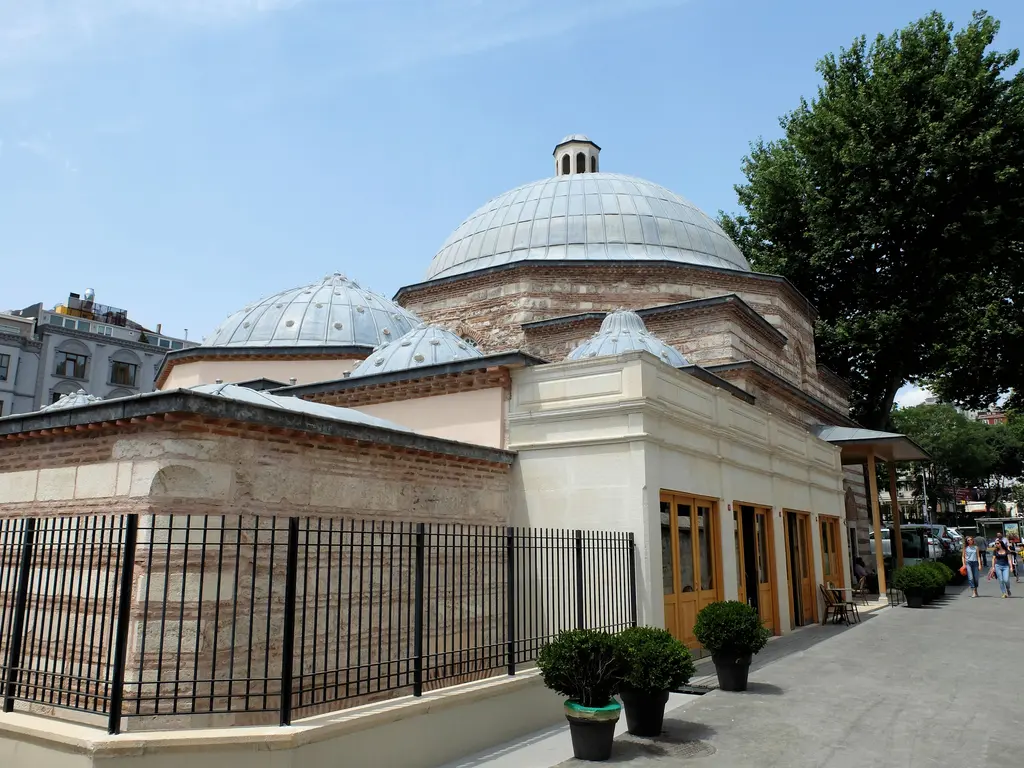 Kılıç Ali Paşa Hamamı; tuğla ve taş duvarlar, kurşun kaplı kubbeler, önde demir parmaklık, saksılar ve ahşap kapılı giriş bölümü.