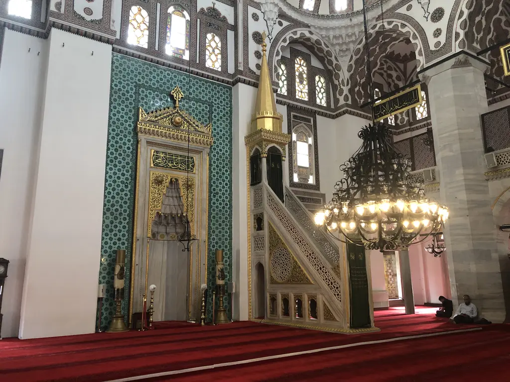 Yeni Valide Camii'nde mihrap ve minber; yeşil çinili mihrap duvarı, yaldızlı minber külahı ve avize.