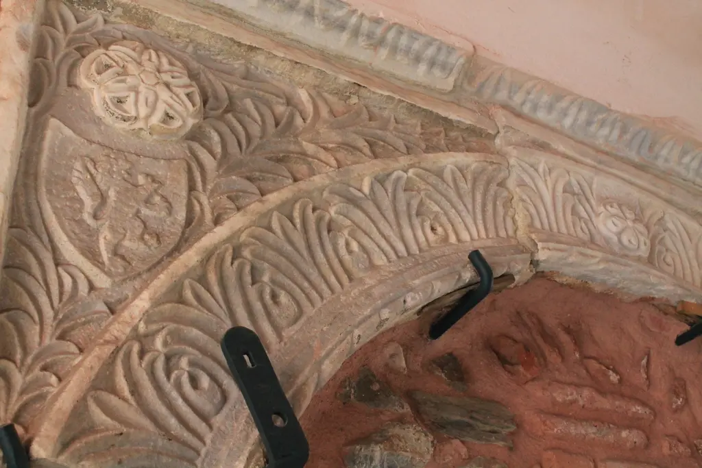 Arap Camii'nde taş kabartma; kırmızımsı yüzeyde kıvrık yapraklar ve hayvan figürlü bir arma parçası.