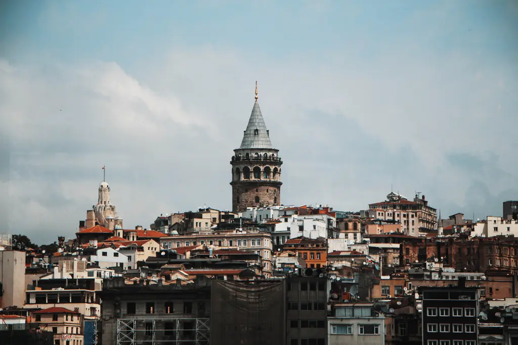 Galata'nın çatıları üzerinde Galata Kulesi; yamaca sıralanan kiremit çatılı apartmanlar, tepede kule ve bulutlu gökyüzü.