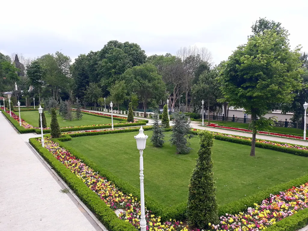 Yıldız Parkı'nda bir bahçe; düzgün biçilmiş çimenler, renkli çiçek tarhları, sivri servi fidanları ve fenerli yollar.