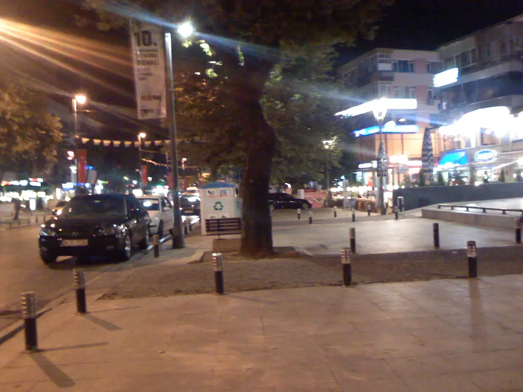Gece Şaşkınbakkal'da Bağdat Caddesi; ışıklı vitrinler, park etmiş araba, kaldırım direkleri ve çınar ağacı.