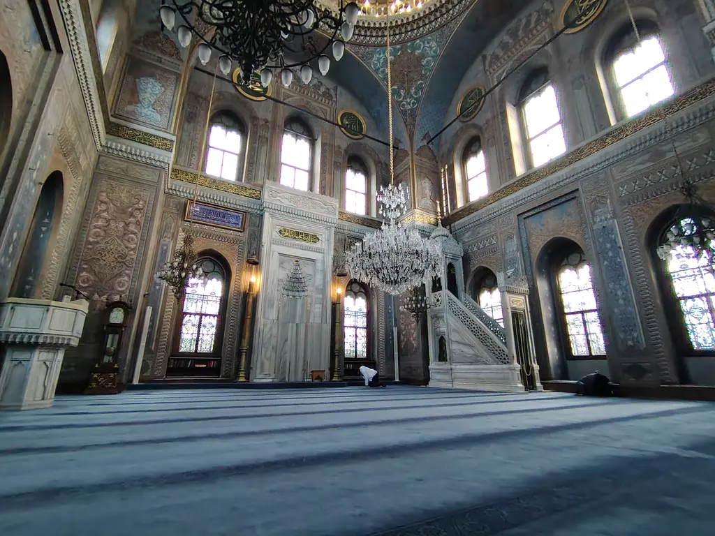 Pertevniyal Valide Sultan Camii'nin içi; mermer minber, avize, mavi halı, yoğun kalem işli duvarlar ve sivri kemerli pencereler.