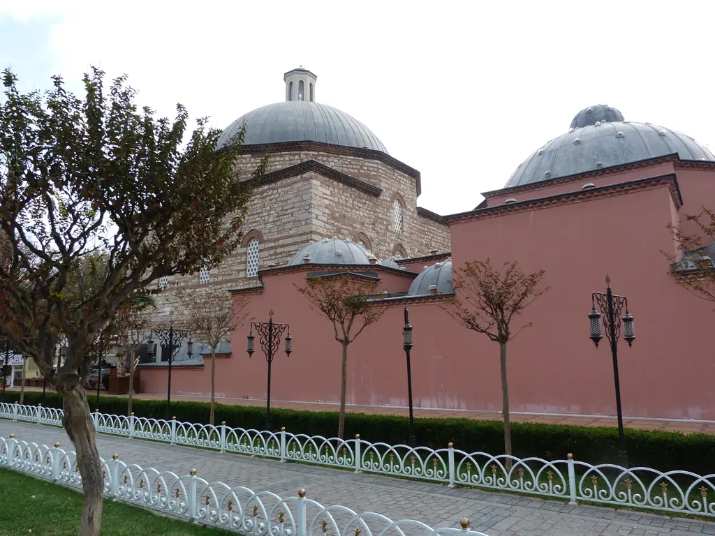 Hamamın park tarafındaki cephesi; pembe boyalı uzun duvar, üstünde üç kubbe, önünde budanmış ağaçlar ve beyaz demir korkuluk.