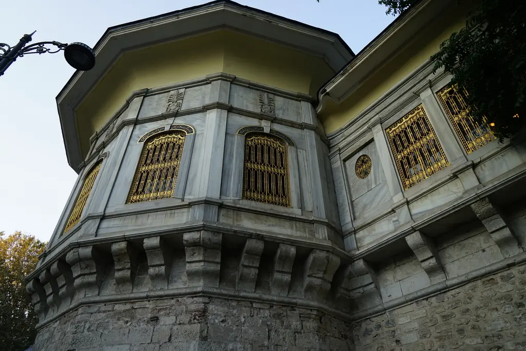 Alay Köşkü'nün cephesine yakından bakış; taş konsollar, mermer kaplama, altın sarısı dökme demir şebekeler ve geniş saçak.