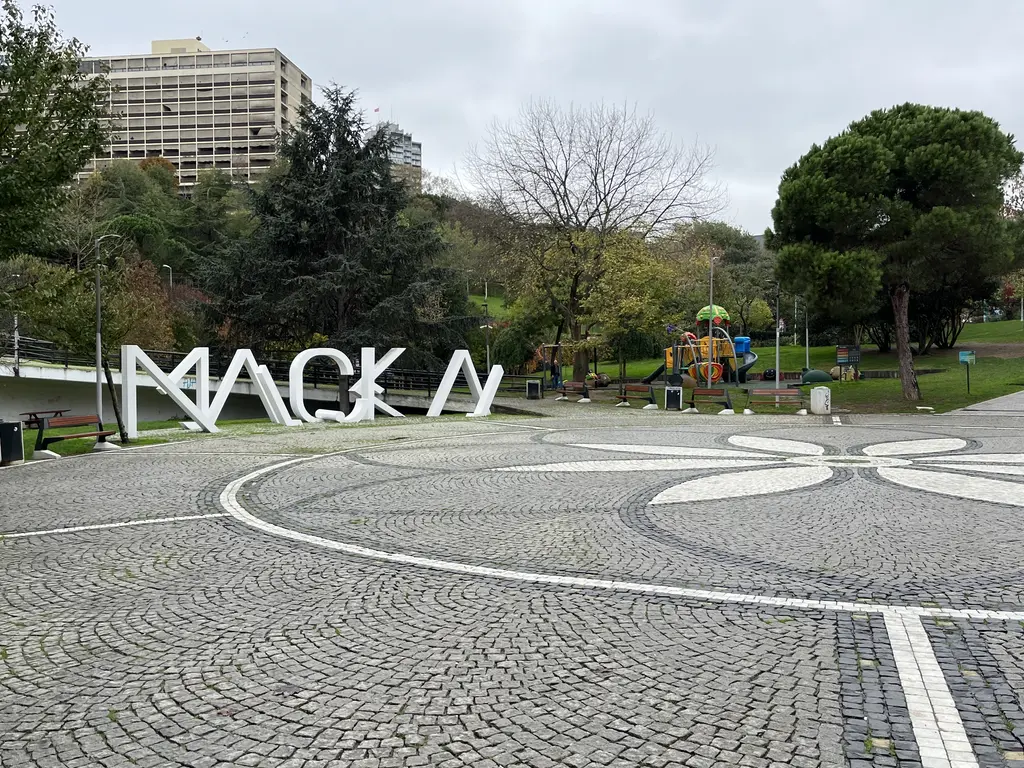 Maçka Demokrasi Parkı'nda beyaz desenli parke meydanda büyük "MAÇKA" harfleri; arkada renkli çocuk oyun alanı, ağaçlar ve bir apartman.