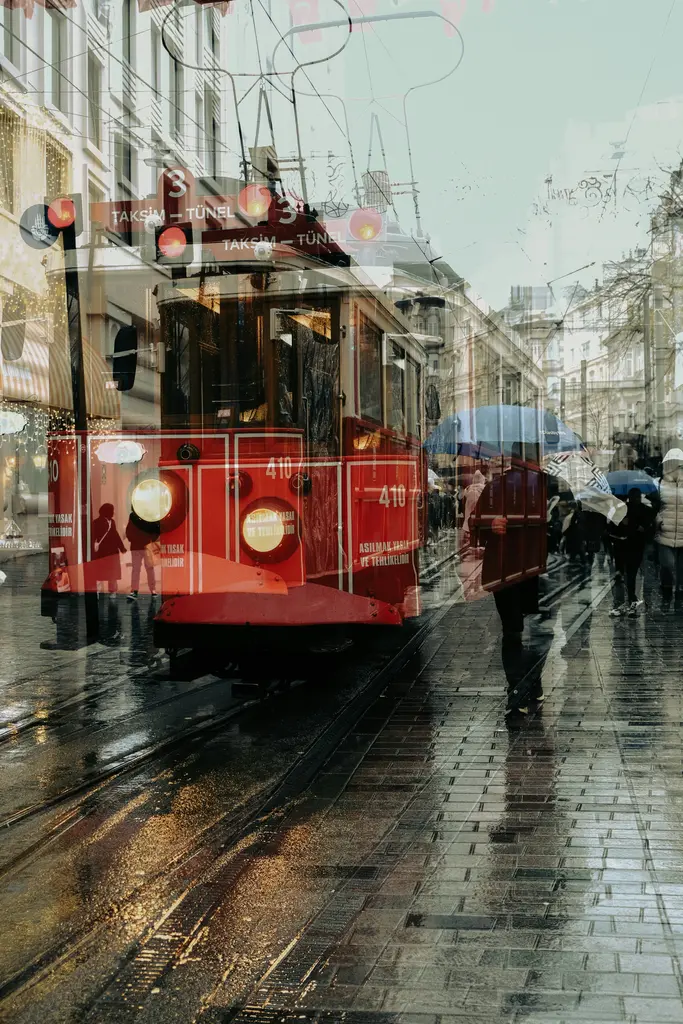 Yağmurlu bir günde İstiklal Caddesi'nde kırmızı tramvay; ıslak taş zemindeki yansımalar ve şemsiyeli yayalar.