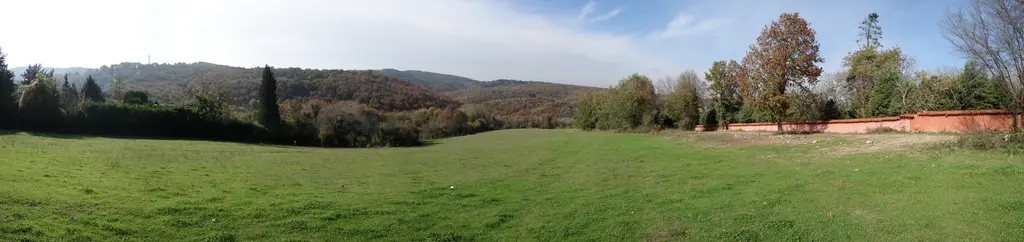 Polonezköy'de geniş biçilmiş çayır, sağda kırmızı alçak bir duvar, sonbahar renkli ağaçlar ve arkada ormanlık tepeler.