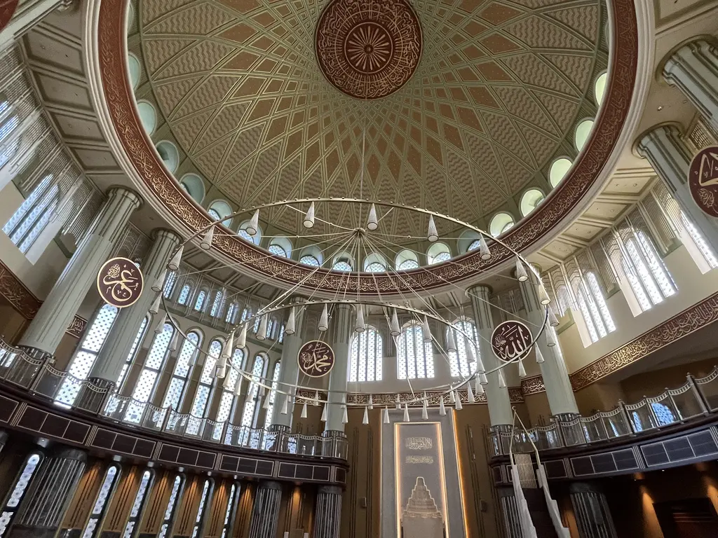 Taksim Camii'nde kıble duvarı; beyaz mermer mihrap, sağında minber, üstte kubbe ve galerilerin pencere dizileri.