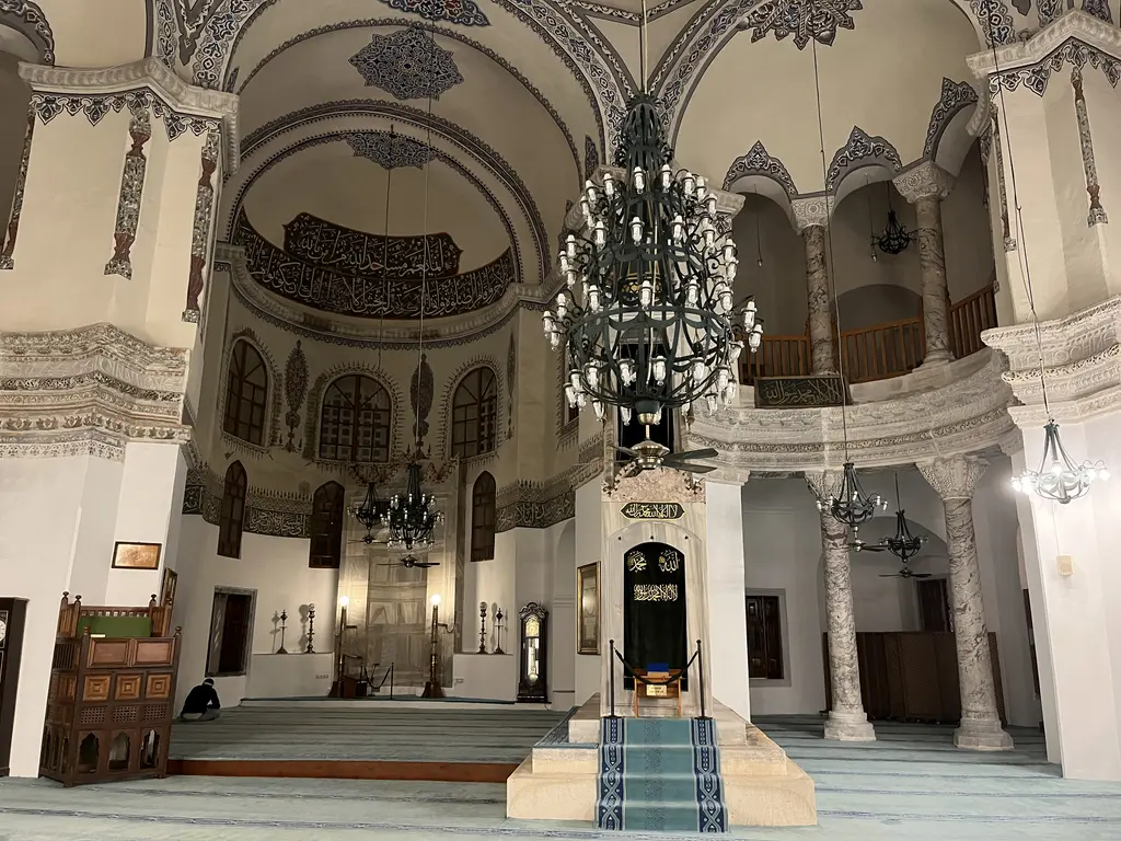 Küçük Ayasofya Camii'nin kıble yönü; ortada apsis ve üstünde geniş hat kuşağı, altta mermer mihrap nişi ile pirinç şamdanlar, solda oymalı ahşap kürsü ve büyük ferforje avize.