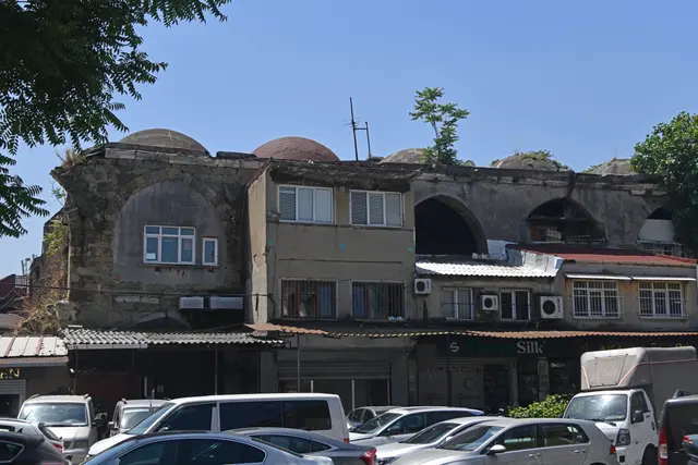 Büyük Valide Han'ın avlu cephesi; sıvası dökülmüş duvarda büyük sivri kemer dizisi, çatıda sıra sıra kubbe, altta dükkânlar ve avluyu dolduran arabalar.