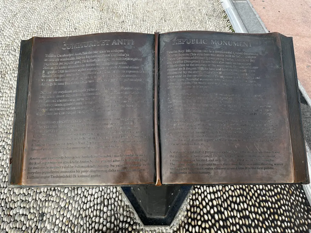 Cumhuriyet Anıtı'nın önündeki bronz açık kitap; sol sayfada Türkçe, sağ sayfada İngilizce yazılar ve çakıl taşı döşeli zemin.