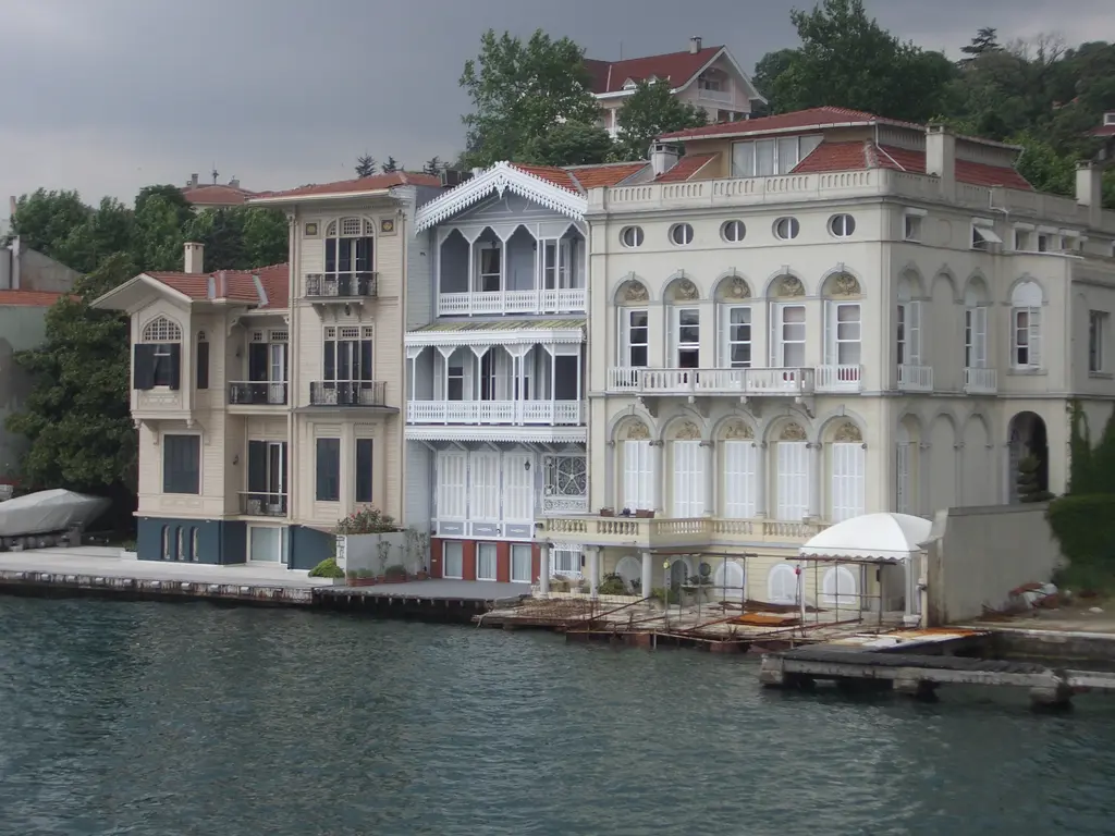 Vapurdan Yeniköy yalıları; beyaz ahşap yalı, kemerli pencereli taş yalı, kiremit çatılar ve önde rıhtım.