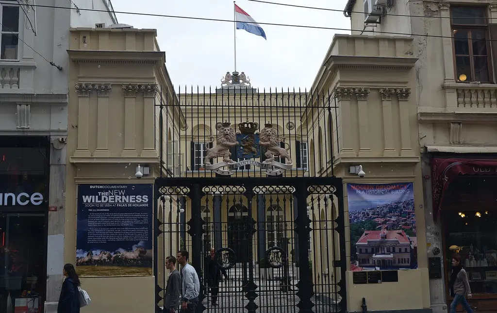 İstiklal Caddesi'nde Hollanda Başkonsolosluğu'nun girişi; armalı taş kapı, siyah demir parmaklıklar ve tepede Hollanda bayrağı.